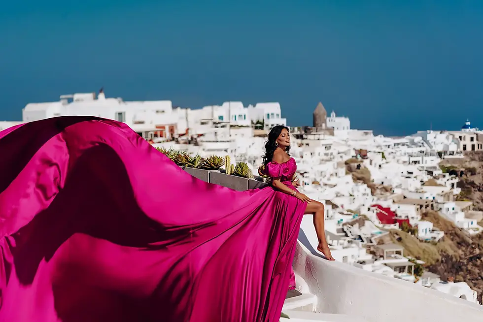 Solo Santorini Flying Dress Photoshoot: woman posing in a flowing fuchsia flying dress overlooking the white cliffs and caldera of Oia, Santorini, Greece.
