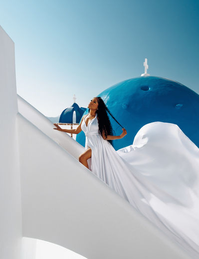 Luxury editorial portrait with flying dress in Oia Santorini near blue domes