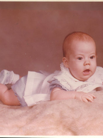 Sweet baby in white dress, lying on pink blanket, looking forward, faded image with major color shift. Unretouched image.
