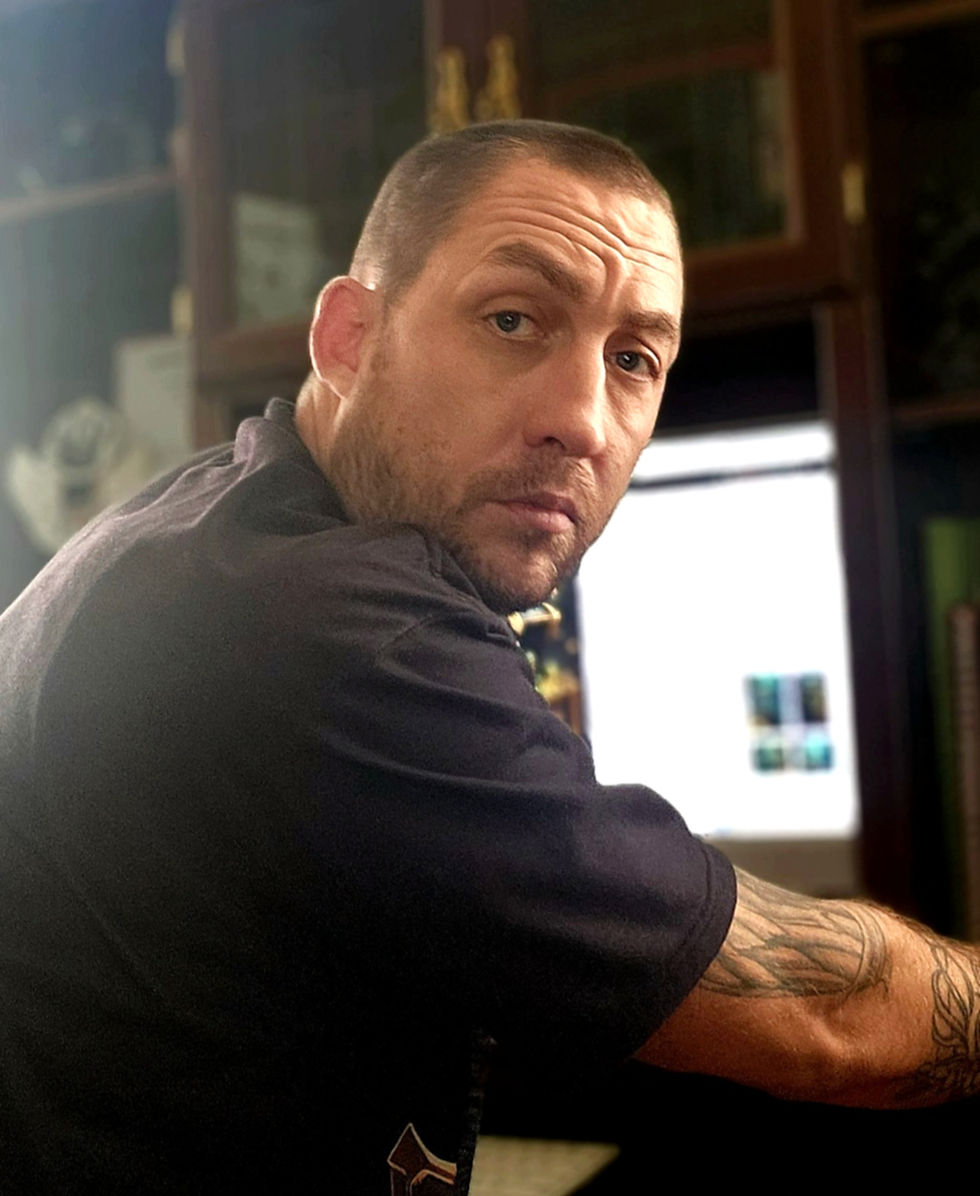 Dragon Head Founder, James, in a black shirt is sitting at his PC as he looks over his shoulder indoors, with a serious, slightly wary expression.