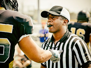 Sports referee with whistle looking at a football player