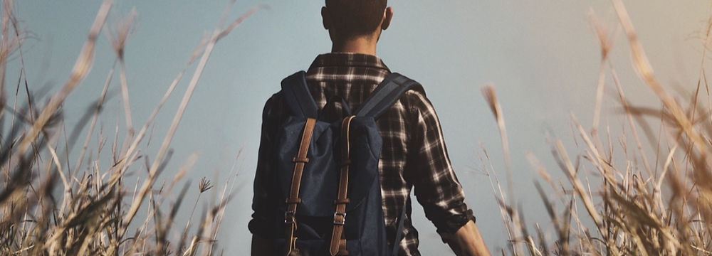 A young man pauses thoughtfully as he considers his options and potential paths ahead of him, while he stands in a field.