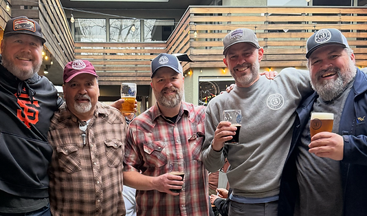 The five founders pose together with their arms around each other in the outside courtyard. They are all wearing hats and smiling with two of them also holding beers.