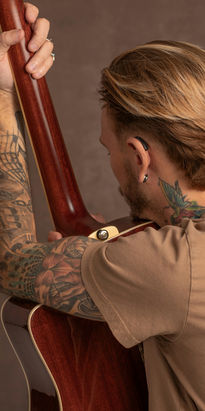 Jonge man met tatoeages houdt een gitaar vast en draagt een hoortoestel