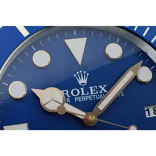 Close-up detail of blue gold Submariner style wall clock showing dial texture, markers, and polished finish
