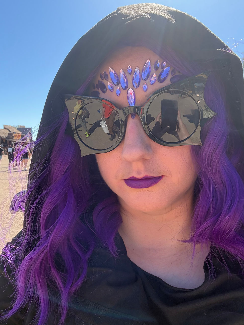 Person with purple hair, hooded cloak, and crafted forehead gems.