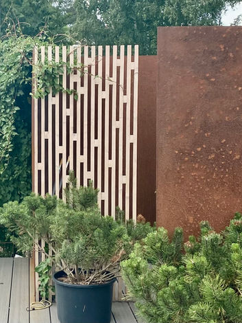 Outdoor shower in corten steel with trellis, small pines in pots, and green climbers