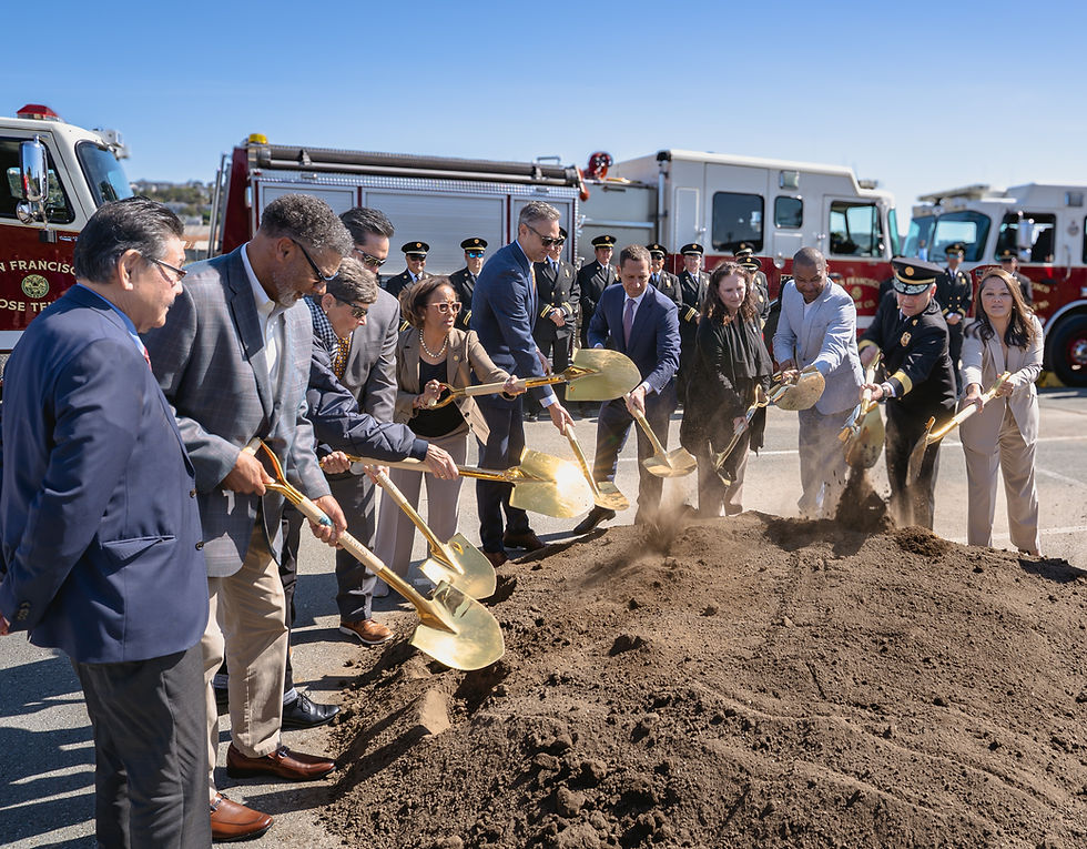 A group of city officials holding golden shovels overturn some dirt on a large dirt pile for a groundbreaking ceremony.