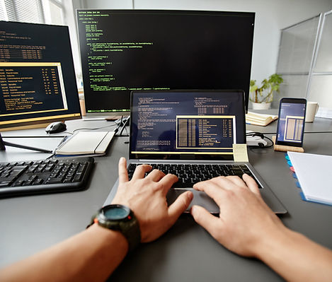 A developer's hands busy at work on a laptop, surrounded by multiple screens displaying code, indicative of testing in CI/CD environments for streamlined software deployment