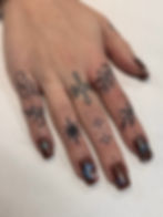 Small handpoke ornamental finger tattoos on a hand with dark nails.