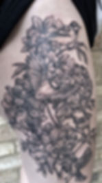 Black and grey floral tattoo with birds on a thigh.