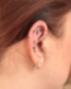Close-up of an ear with small black ink handpoke tattoos and piercings.
