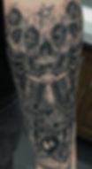 Detailed skull and pentagram tattoo with script text.