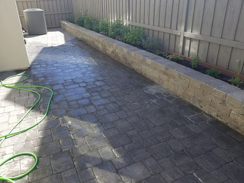 Paved backyard with retaining wall and garden bed by enovation landscaping