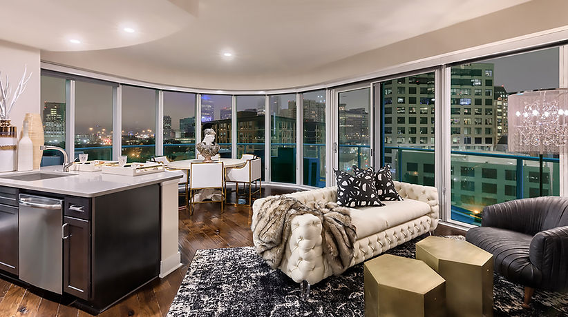Corporate housing in Dallas: living room with a tufted sofa, dining set and curved floor-to-ceiling windows over city lights