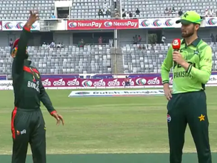 Bangladesh and Pakistan cricket captains during the coin toss before a match in a stadium, with the Bangladesh captain tossing the coin and the Pakistan captain holding a microphone.