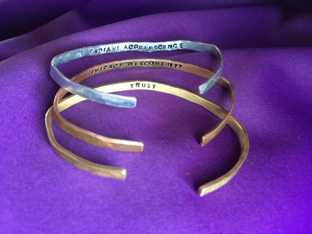 bracelets with the words radiant acquiescence, embrace discontinuity, and trust.