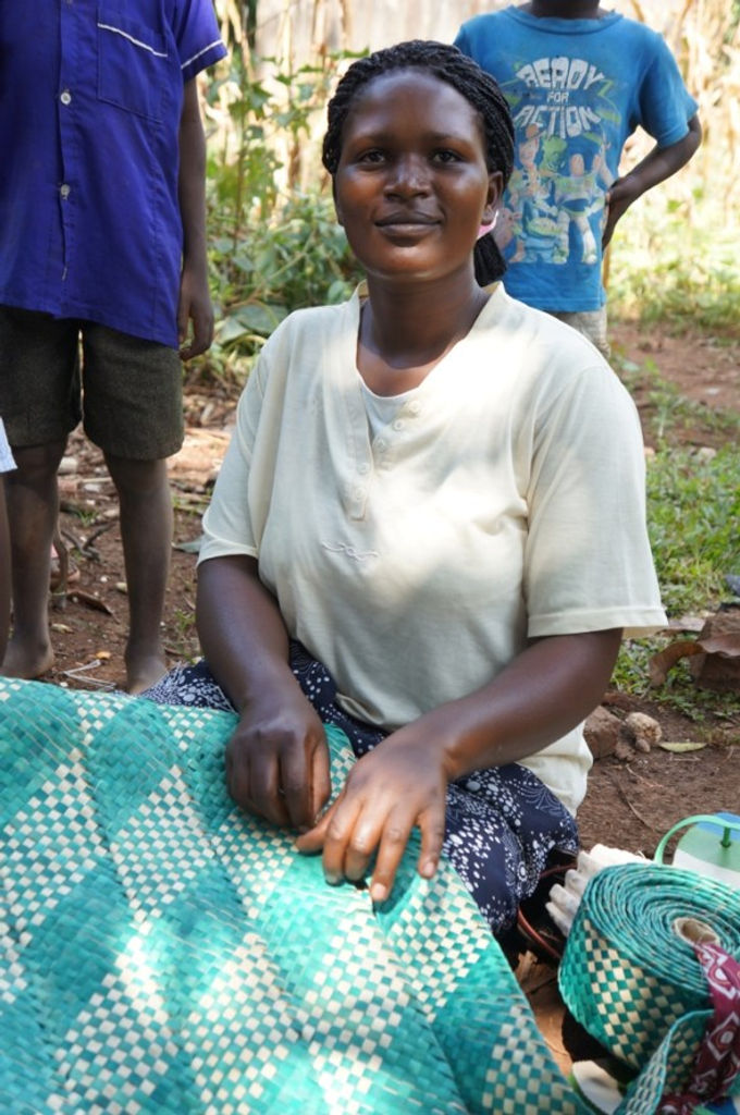 Ruth shows us one of the mats she's made to sell. Before the Small Business Fund grant the family was just subsistence farming, now their farm has grown so that they have enough to sell. (Uganda)