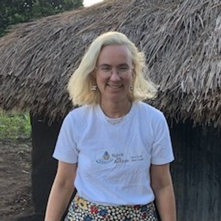 Tanya wears a Spirit in Action branded shirt and smiles in front of a thatched home in Uganda.