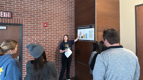 C4Y staff member presents a poster on "Sleep Protects Teens from Depression" to a group of people in a brick-walled room. Attendees listen attentively.