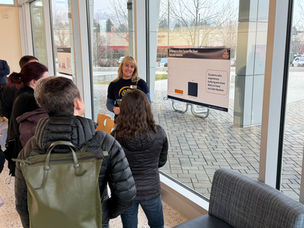 Group of people listening to a C4Y staff member presenting a chart on bullying and teen mental health in a bright indoor setting with glass windows.