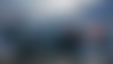 Cyclists and spectators gather in a mountainous parking area. People smile and give thumbs up. Snow-capped peaks in background.