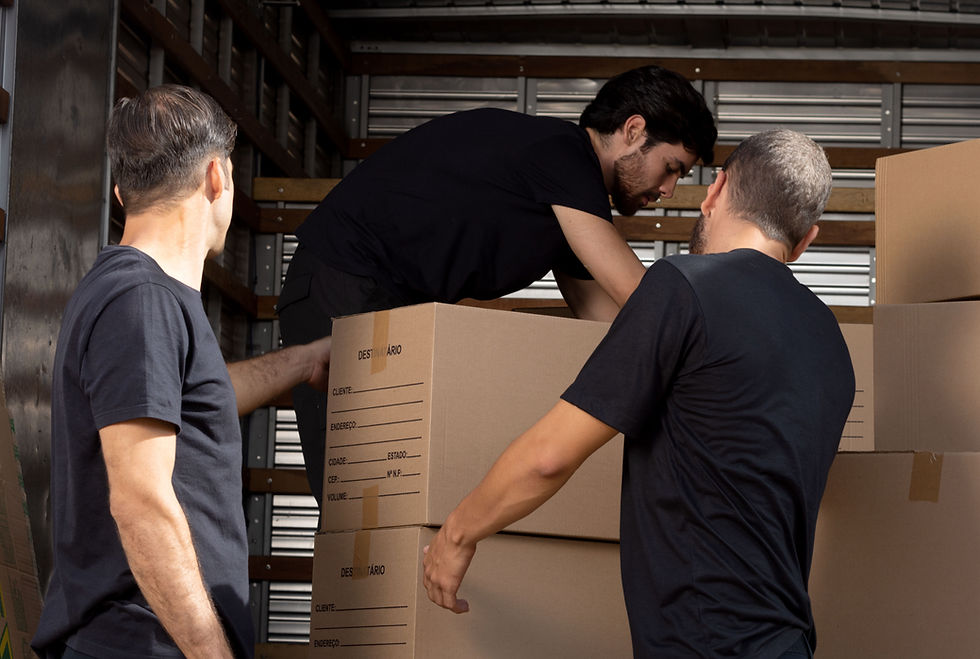 Group of 3 men in black shirts moving cardboard boxes out of the back of a moving truck.