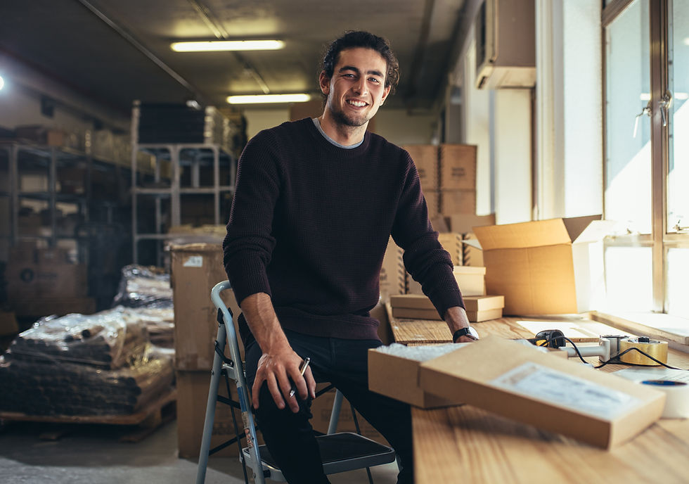 Man sitting on the top step of a step ladder, packing a box and writing a label for it.