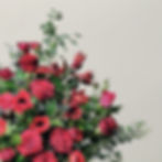 Détail d’un bouquet rouge : roses velours, mini-amaryllis et feuillages aériens sur fond clair.