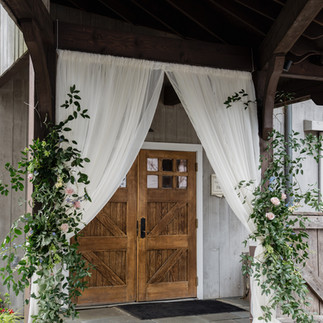 Ceremony entrance with white draping and greenery over wooden doors, creating a romantic 2026 wedding trend loo