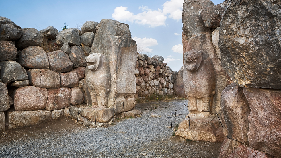 Stone lion statues flank a narrow gravel path between huge rock walls under a blue sky with clouds.