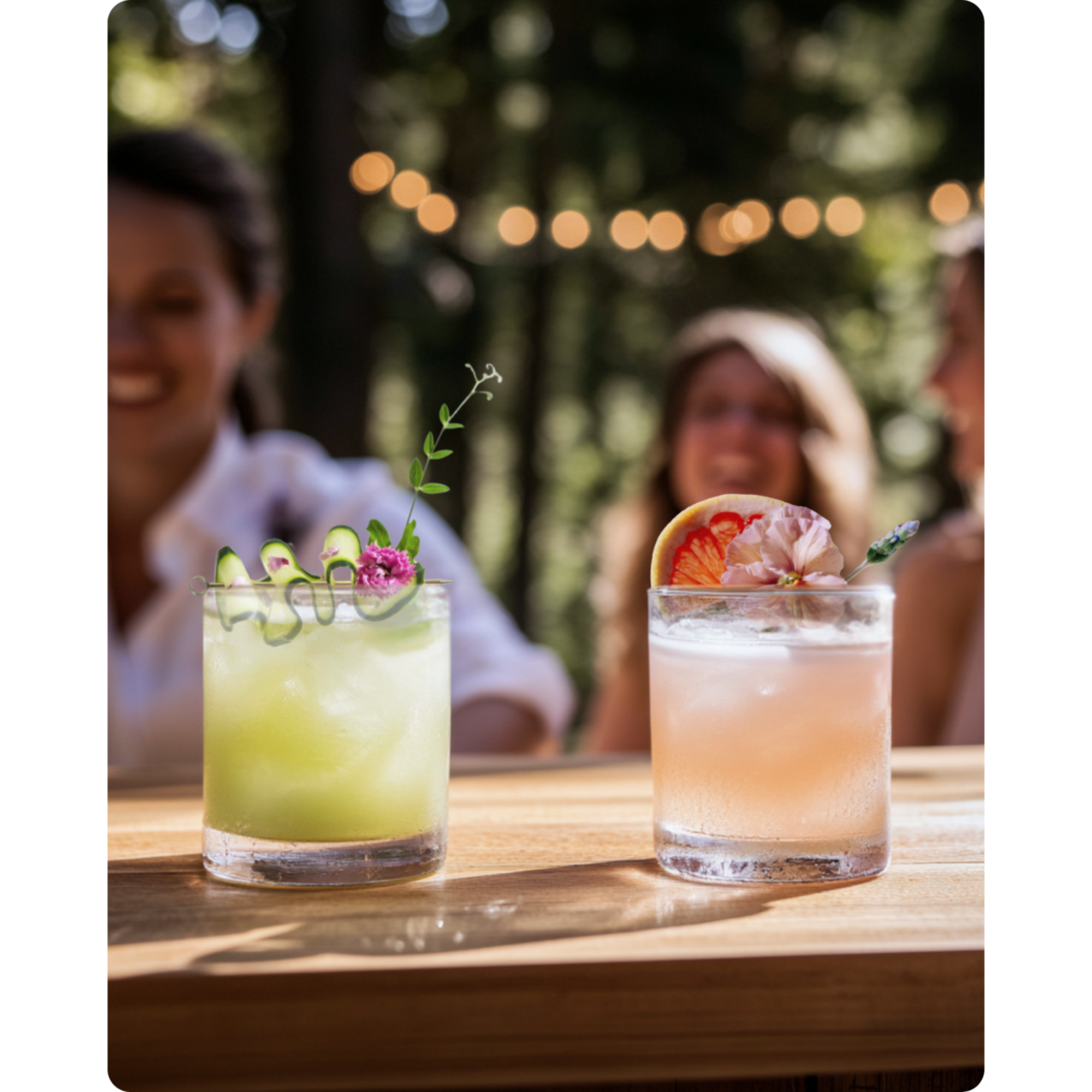 Two garnished cocktails on a wooden bar at an outdoor gathering