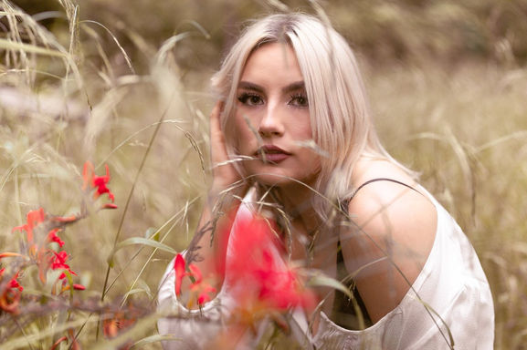 Portrait of blonde female model sat down in a field looking at camera at Parc Cefn Onn in Cardiff