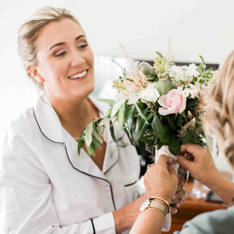 Mother of bride hands her daughter bouquet of flowers on wedding morning