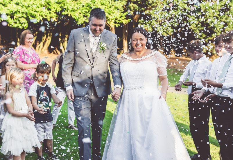 Bride and groom smiling holding hands while walking during confetti throw on wedding day in garden at Manor Parc Country Hotel in Cardiff