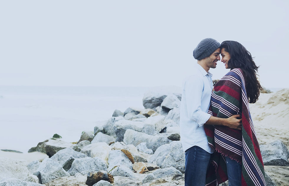 Couple smiling at each other while touching heads together as they stand near rocks during engagement photoshoot