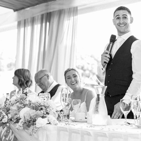 Groom in the middle of his speech while bridal party laugh at the top table
