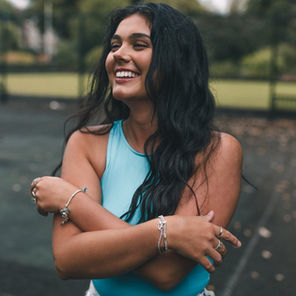 Portrait of brunette female model smiling in tennis court wearing blue top at Roath Park in Cardiff