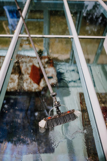 Cleaning a glass roof with a long-handled brush.