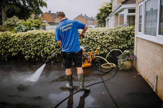 A professional power washing a driveway outside a house.