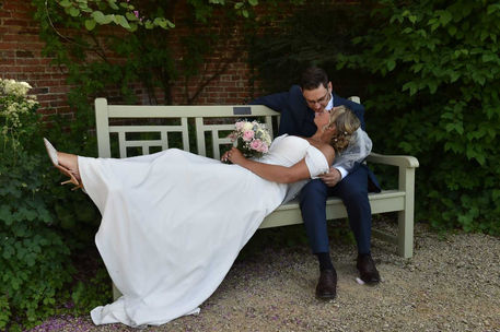 Newlywed couple posing on a bench. The bride laying down with her head in the grooms lap