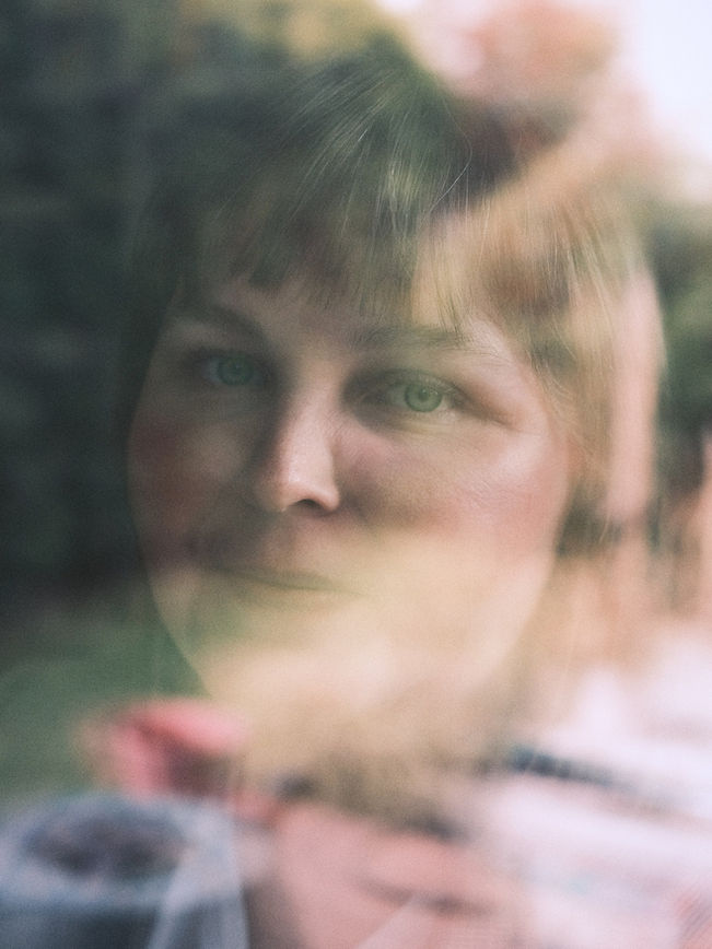 Frau hinter einer Fensterscheibe mit grünen Spiegelungen, weiches Farbportrait
