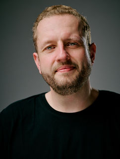 Portrait eines Mannes mit blondem Bart und schwarzem Shirt vor graugrünem Hintergrund