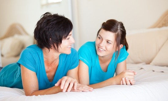middle aged mother and teen daughter chatting on bed