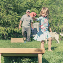 Young girl playing cornhole outside in the sun