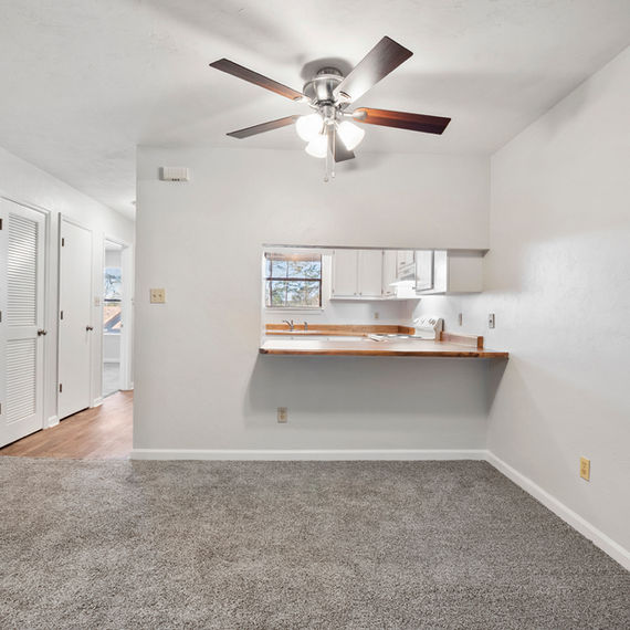 Dining room with carpet, a counter, and a ceiling fan, white walls.