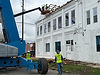 Workers on a lift and ground demolishing white building