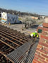 Construction worker on roof demolishing exposed joists overlooking a town.