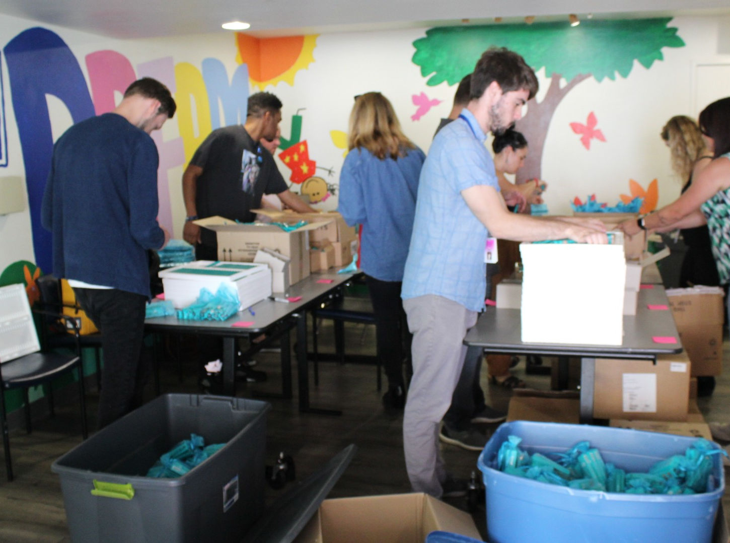 Volunteers organizing and packing donation items in colorful UBH community room with organization banner visible