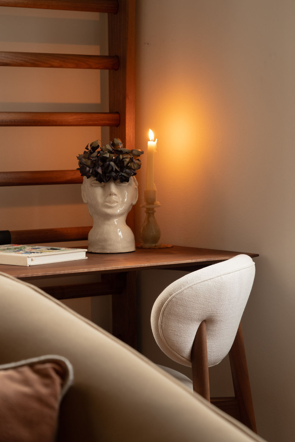 Writing nook detail at the Lake Residence with ceramic head vase, lit candle, book, and Bassam Fellows chair against a wood desk.